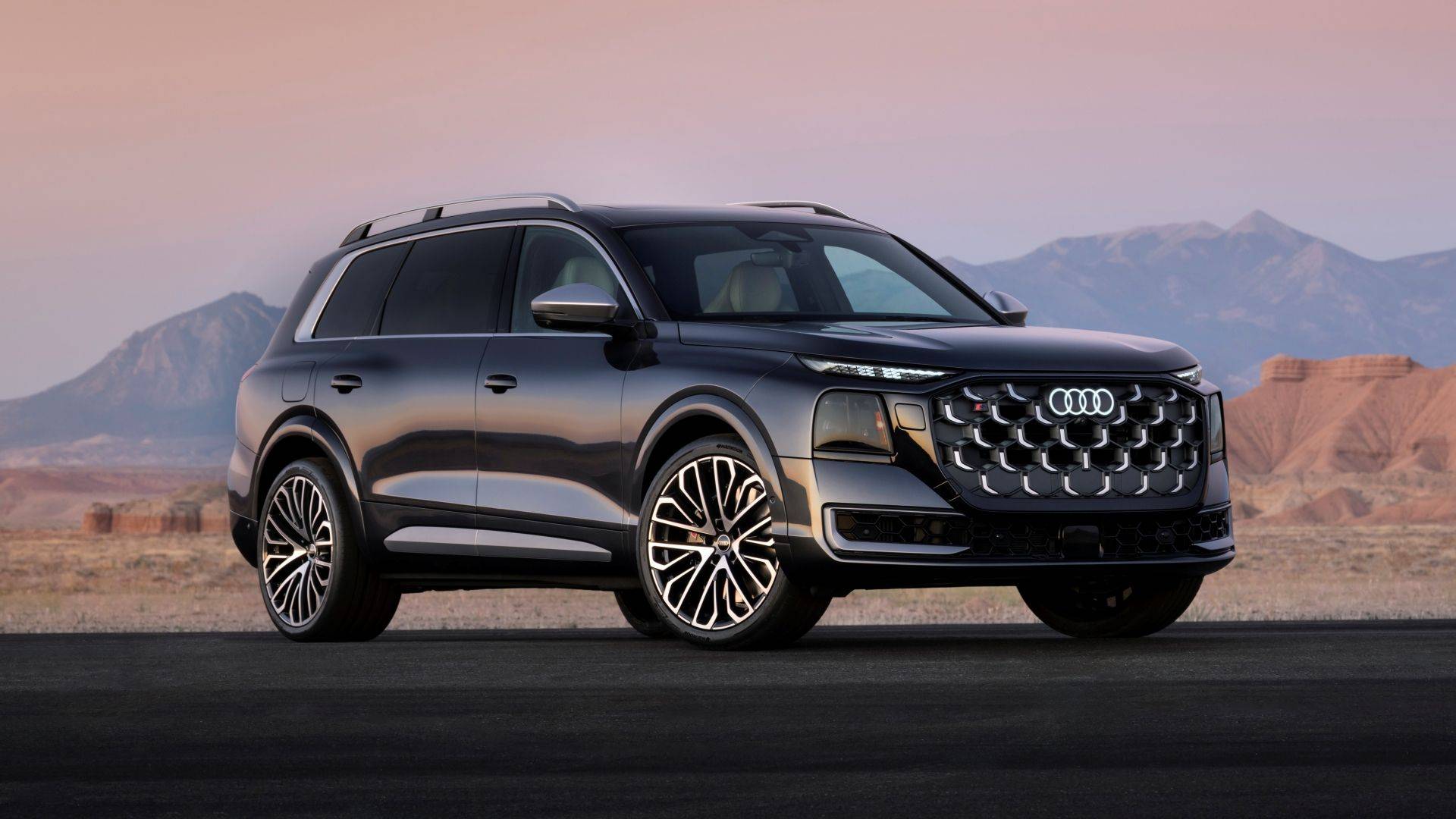 Dark Audi SQ9 SUV parked on a road in a desert landscape with mountains behind it.