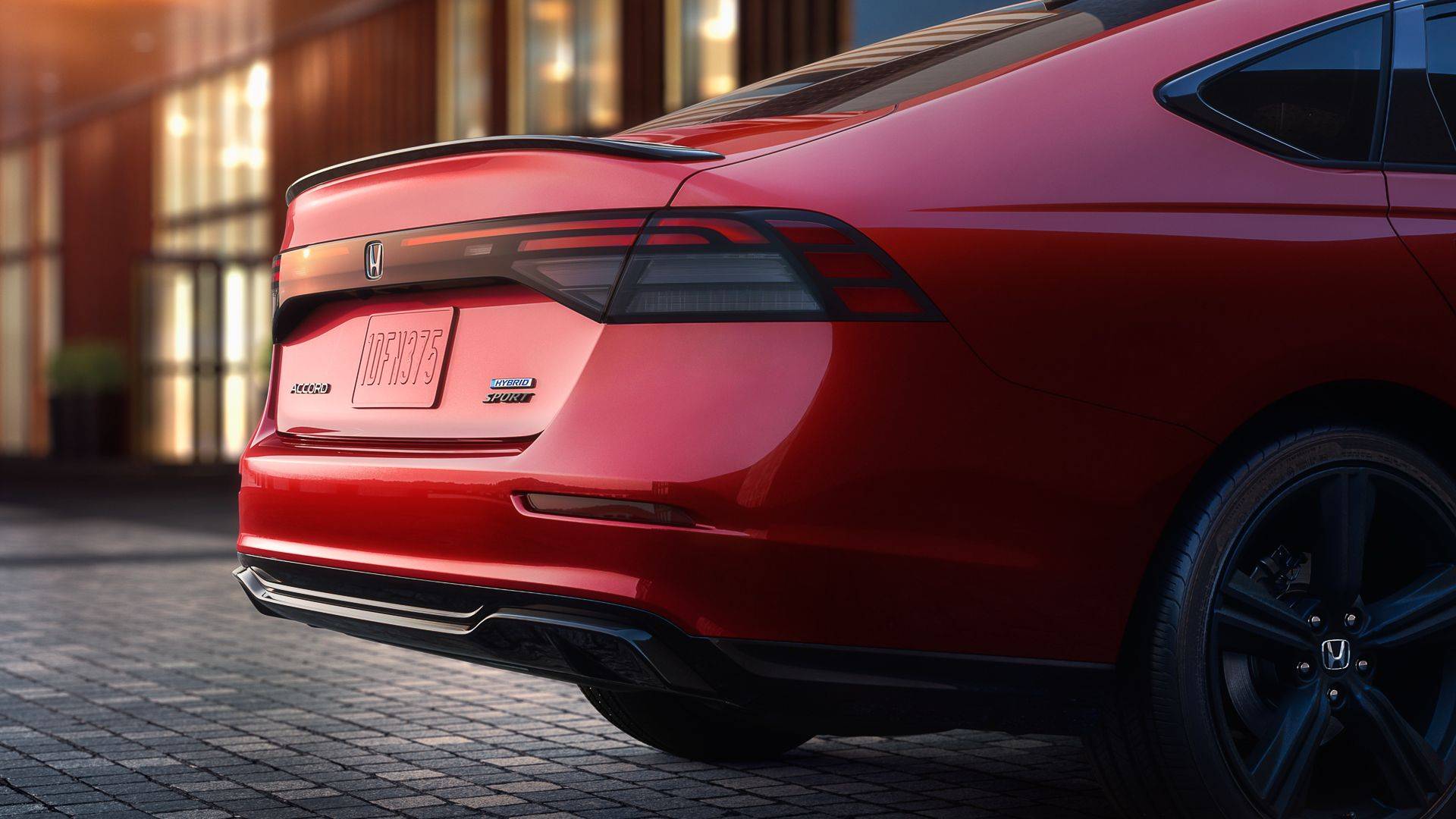 Rear close-up of a red Honda Accord Hybrid Sport sedan with black wheels and trunk spoiler.