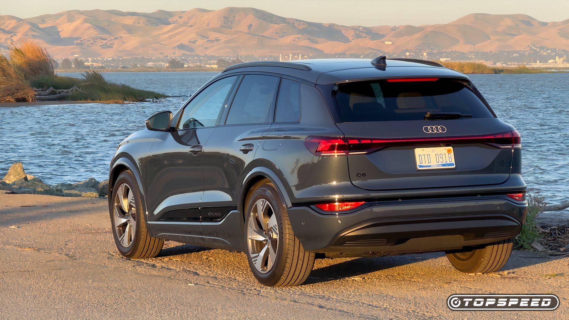 Rear three-quarter view of the Audi Q6 e-tron electric SUV parked beside water