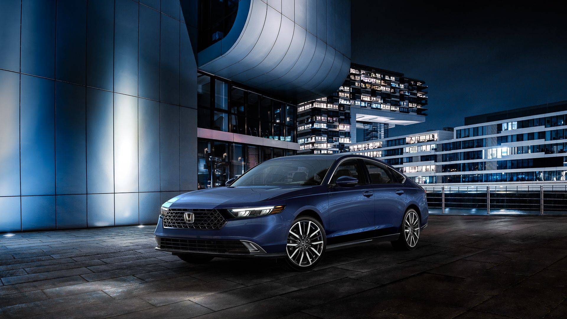 Blue 2024 Honda Accord sedan parked at night outside modern city buildings.