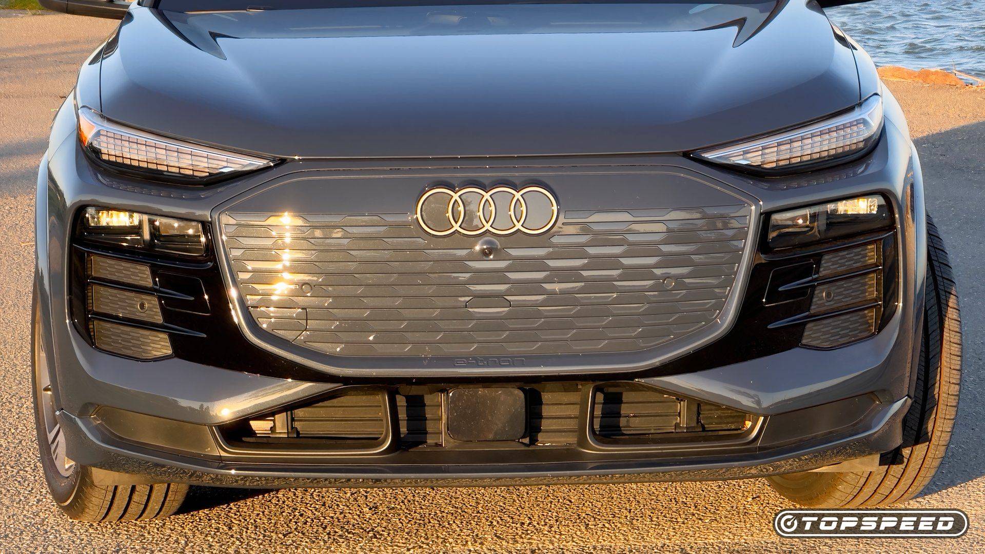Front close-up of a gray Audi Q6 e-tron with Audi rings, closed grille, and LED lights
