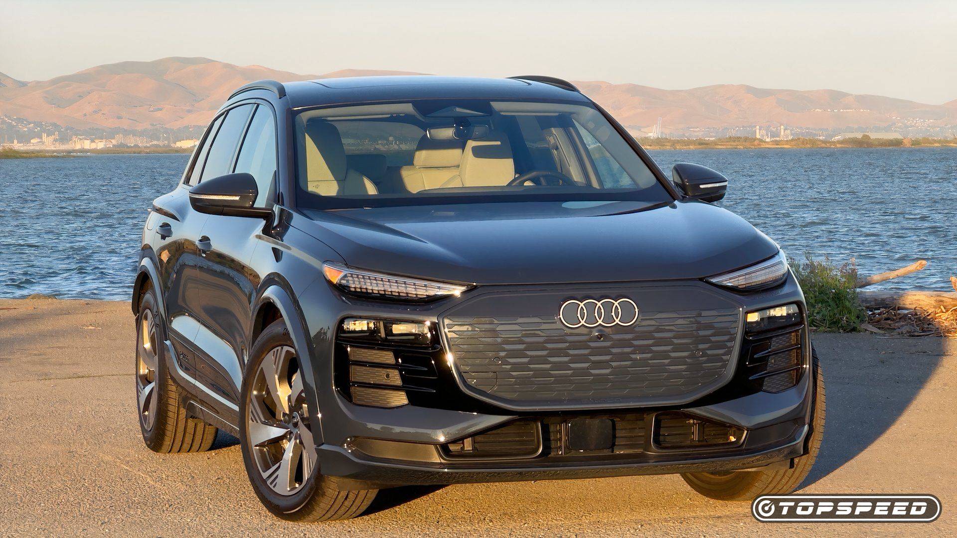 Dark Audi Q6 e-tron electric SUV parked beside water with hills in the background
