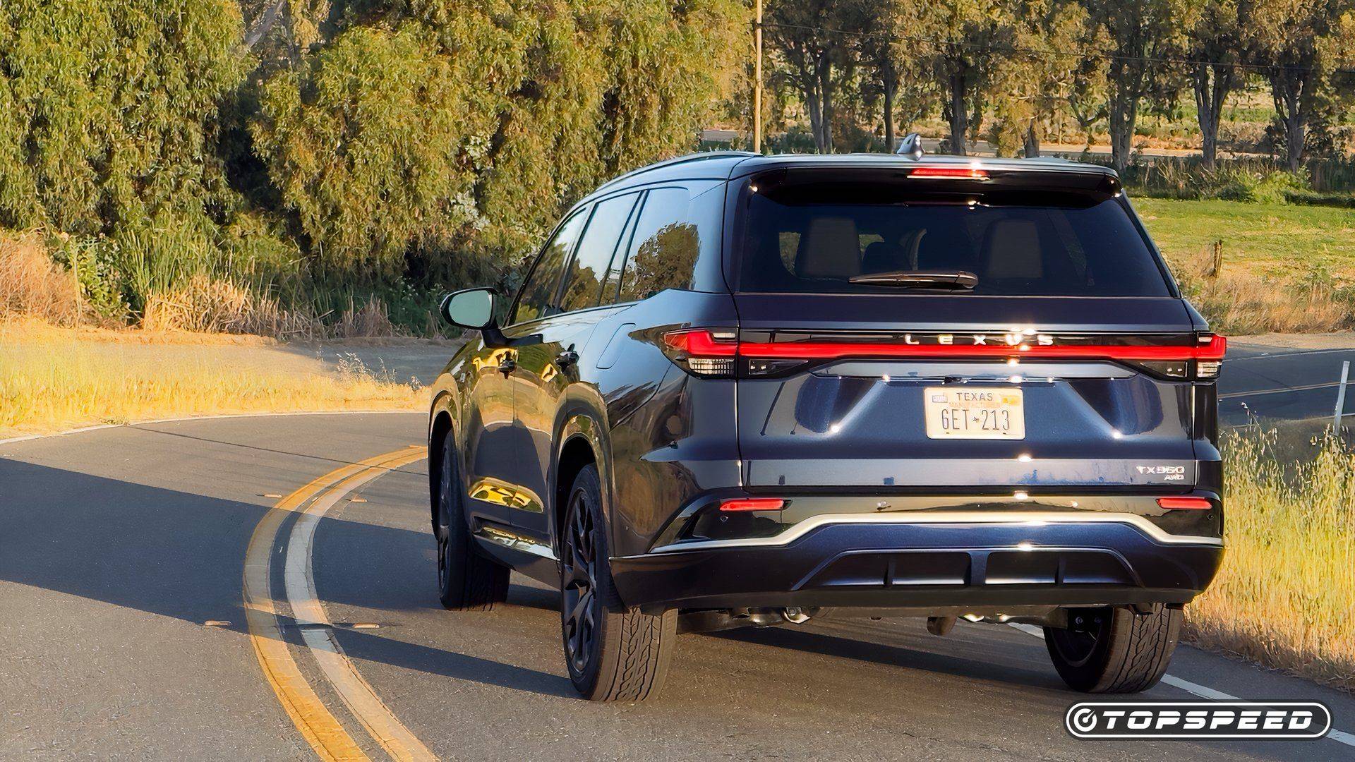 Dark Lexus TX 350 F Sport AWD driving away on a winding road