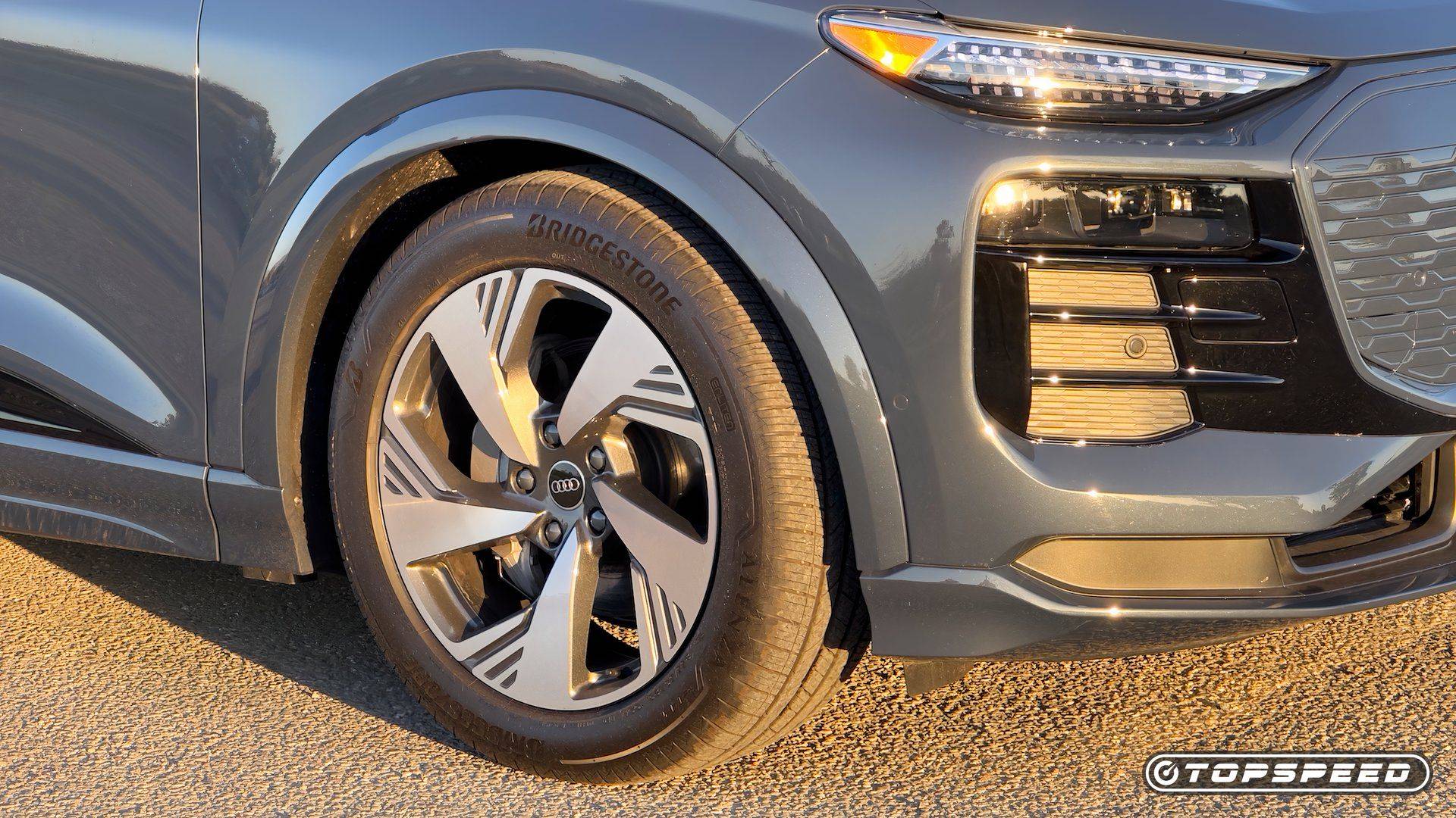 Close-up of a gray Audi Q6 e-tron front wheel, tire, grille, and illuminated headlight