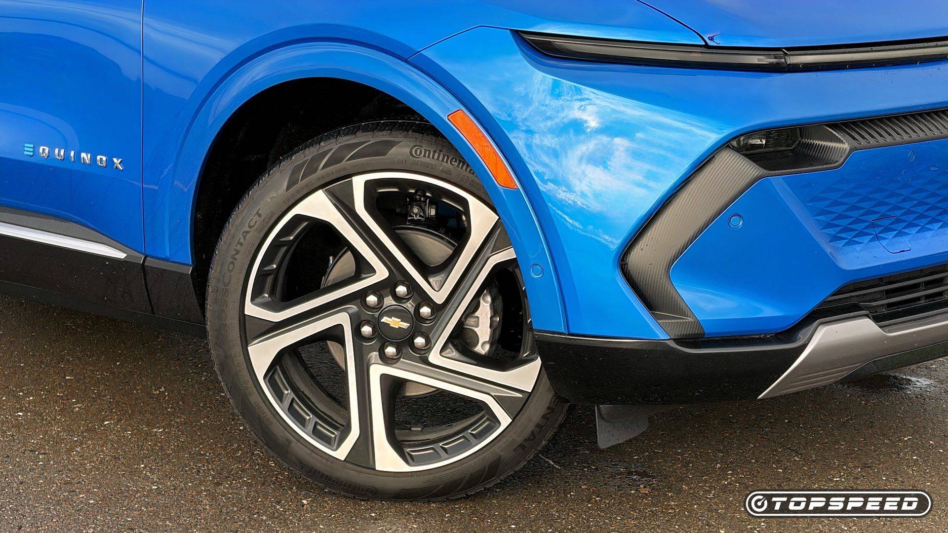 Close-up of the front wheel and bumper of a blue Chevrolet Equinox EV with the Equinox badge visible.