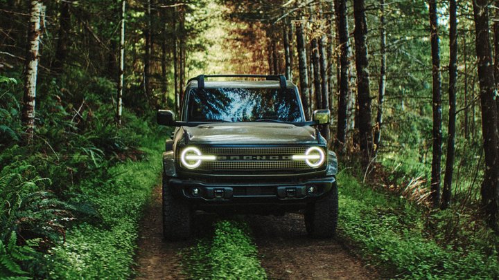 Ford Bronco Filson with illuminated headlights on a narrow woodland trail
