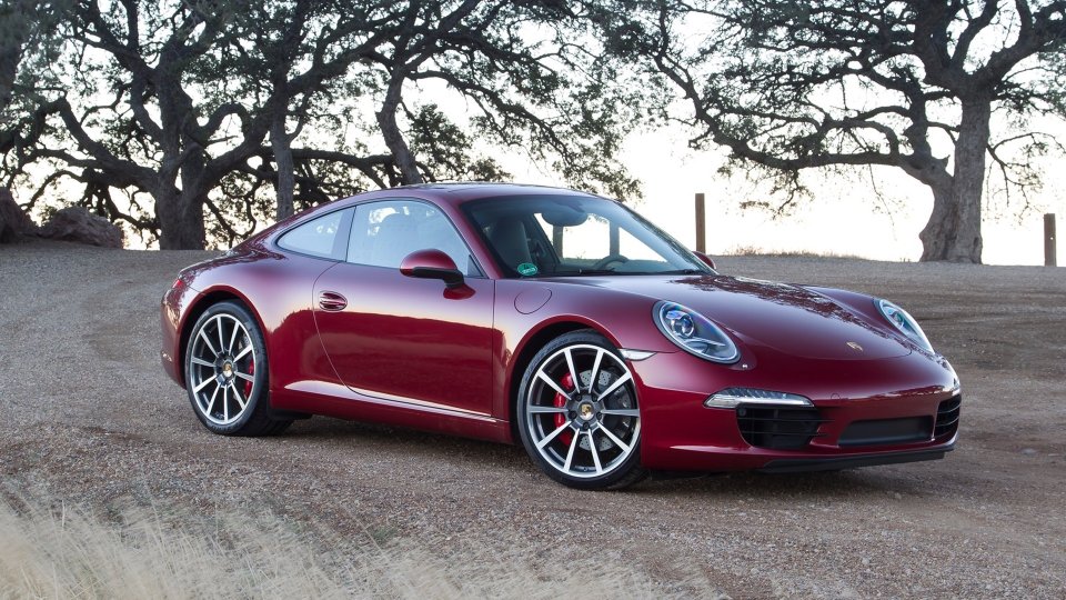 Red Porsche 911 Carrera S parked beneath trees, viewed from the front three-quarter angle