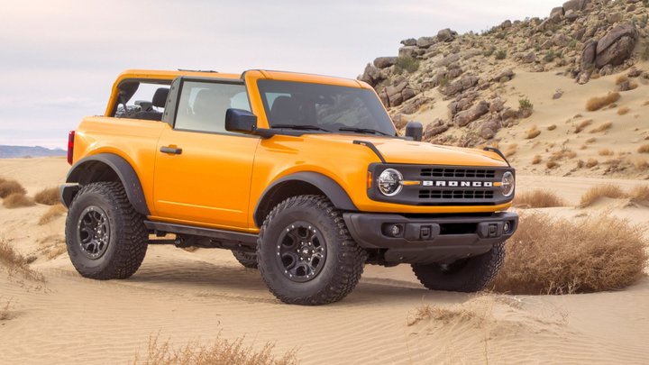 Orange 2021 Ford Bronco two-door with roof panels removed on a sandy desert trail