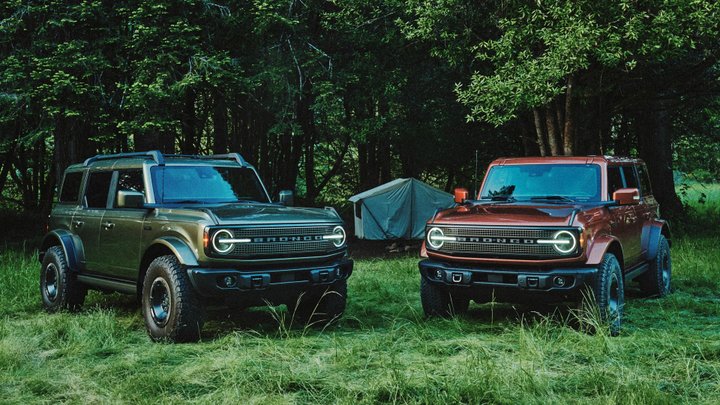Olive green and copper Ford Bronco Filson SUVs parked beside a tent in the woods