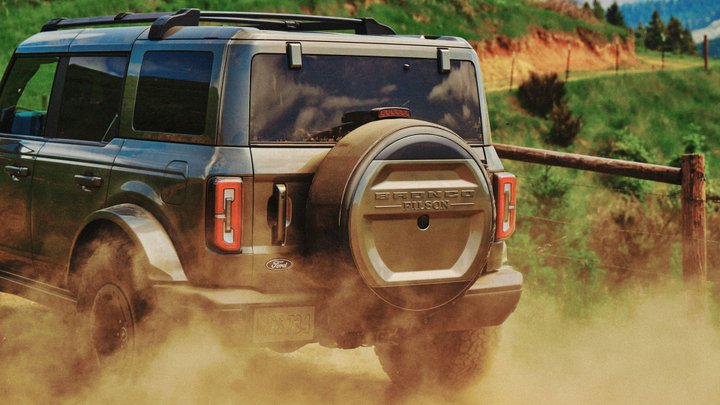 Ford Bronco Filson driving through dust beside a wooden fence
