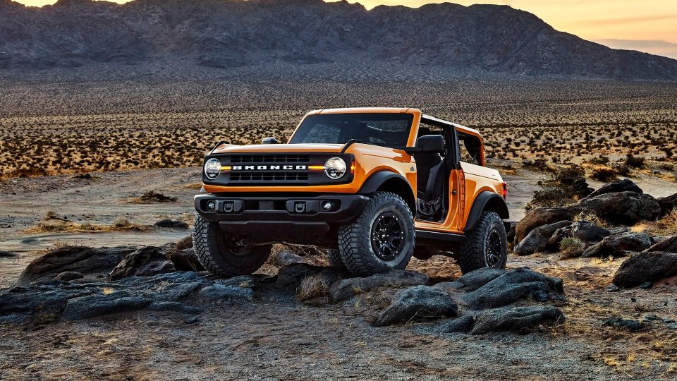Orange two-door Ford Bronco driving over rocks in a desert landscape