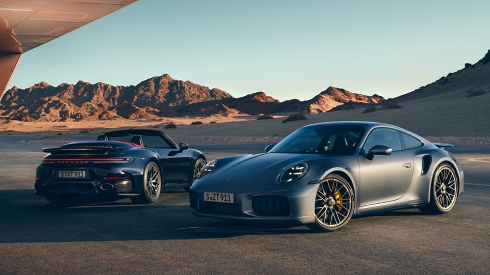 Silver Porsche 911 Turbo S Coupe with a dark 911 Turbo S Cabriolet against a desert mountain backdrop