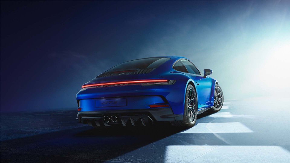 Rear three-quarter view of a blue Porsche 911 GT3 with a Manthey Kit in a dramatic studio