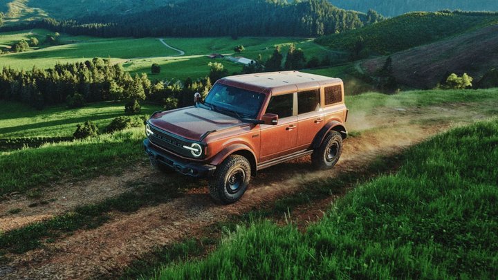 Bronze Ford Bronco Filson driving on a dirt track through a green hillside