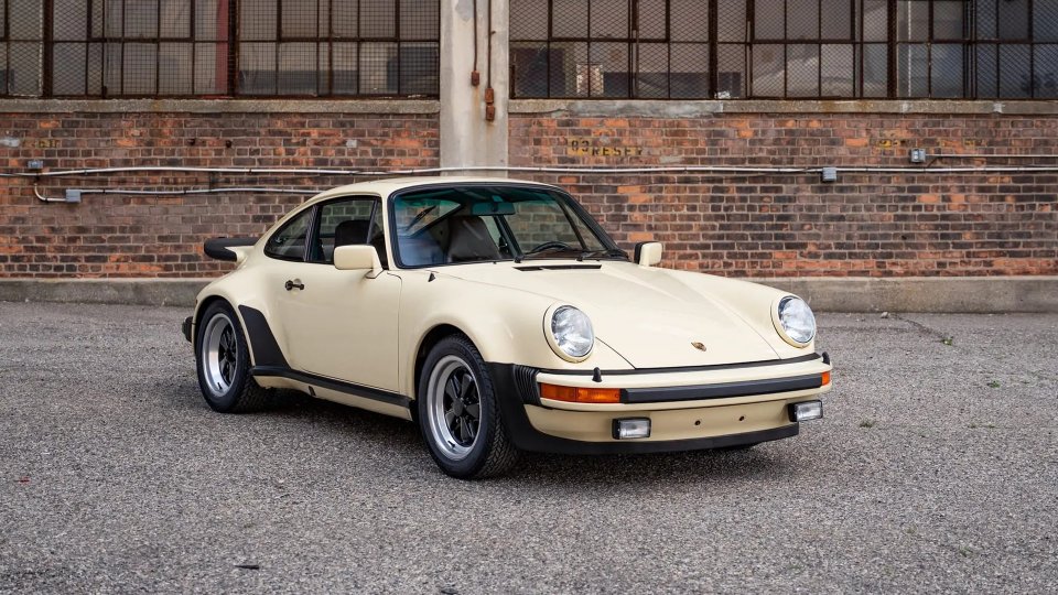 Cream-colored 1977 Porsche 930 Turbo Carrera parked in front of a brick building