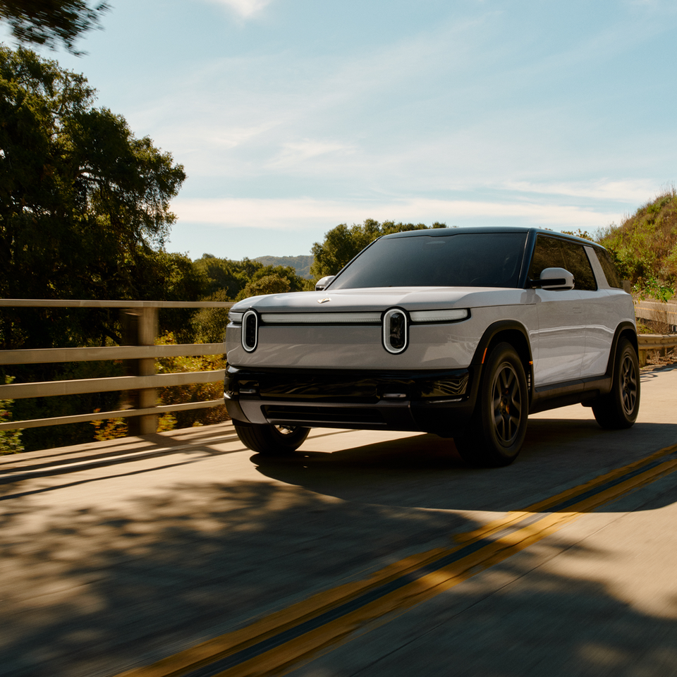 White Rivian R2 electric SUV driving on a winding road