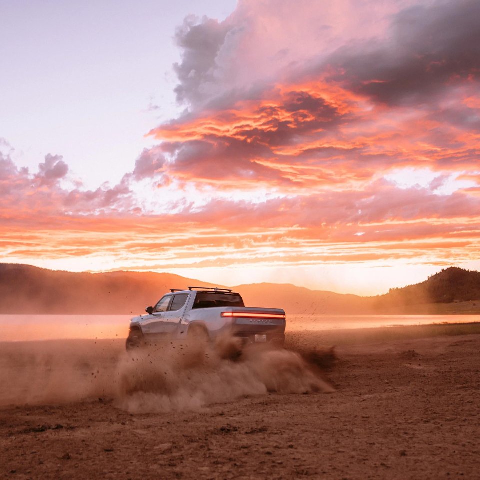 Rivian R1T electric pickup driving on a dusty road at sunset