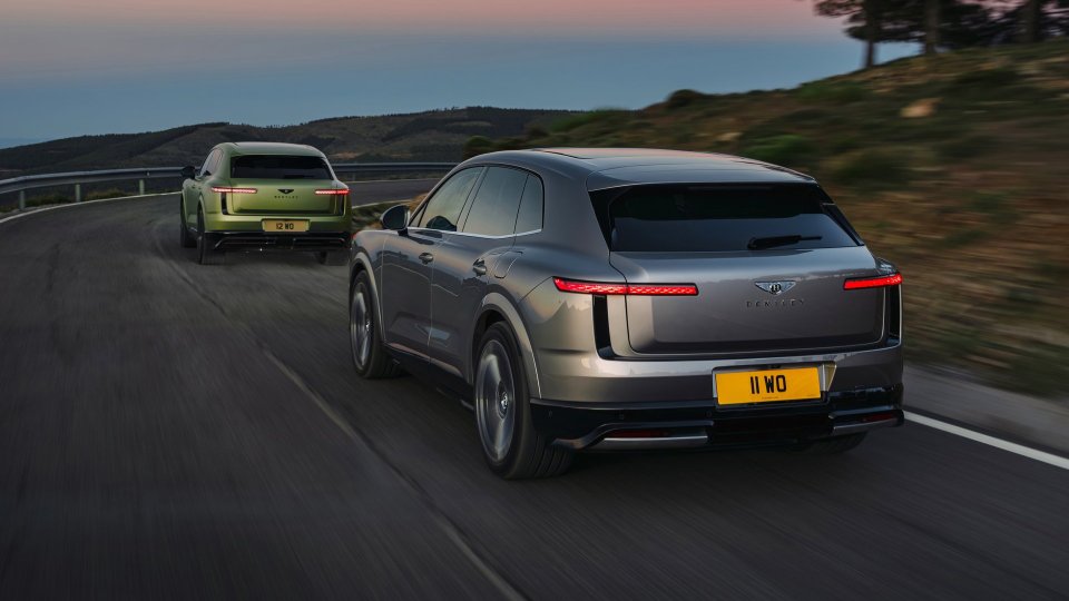 Gray and green Bentley Torcal electric SUVs driving on a winding road at dusk