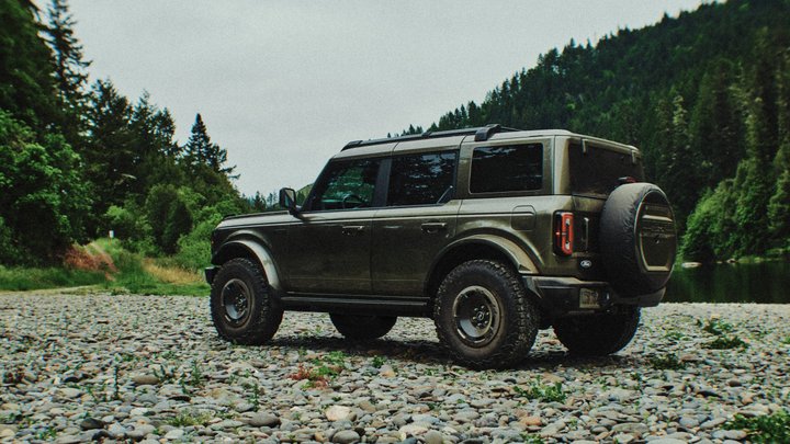 Side view of a dark green Ford Bronco Filson on a forest trail