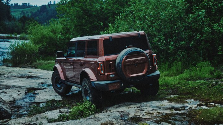 Burgundy Ford Bronco Filson from the rear on a wet rocky forest trail