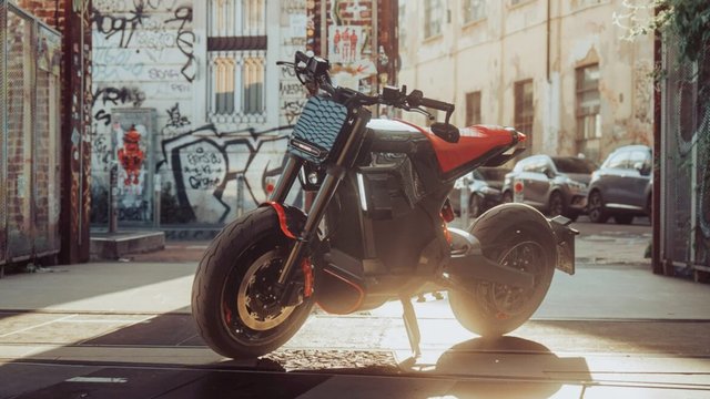 Red-and-black DAB x BRABUS Urban E First Edition electric motorcycle in a graffiti-covered city alley