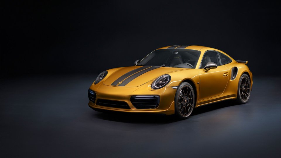 Gold Porsche 911 Turbo S Exclusive Series with carbon-fiber stripes in a dark studio