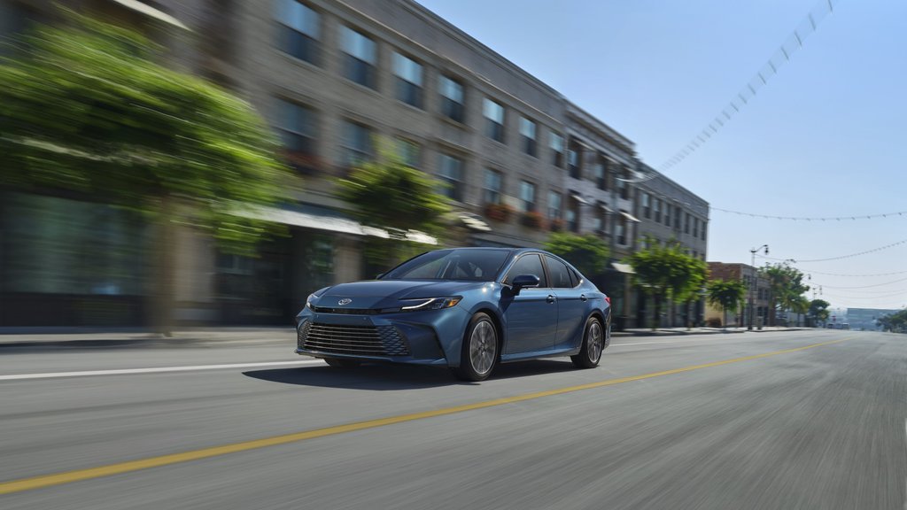 Blue Toyota Camry driving on an urban road.