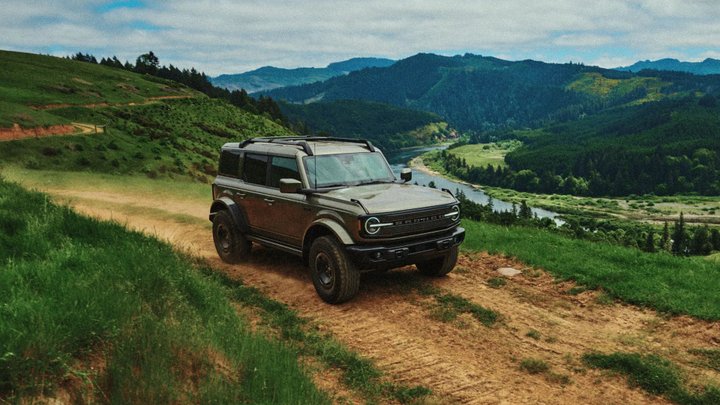 Dark green Ford Bronco Filson on a dirt track above a river valley