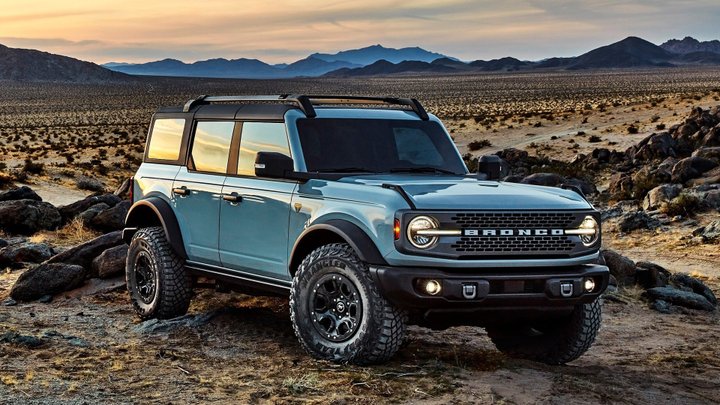 Blue 2021 Ford Bronco four-door with headlights on in a rocky desert landscape